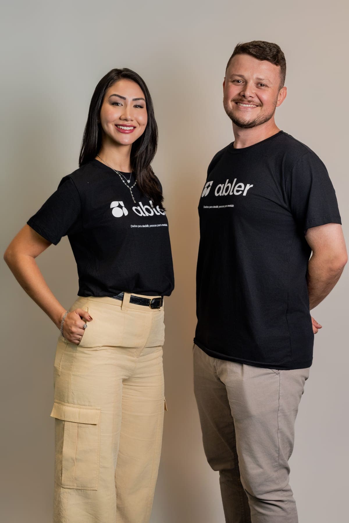Duas pessoas do time da abler lado a lado, sorrindo, vestindo camisetas pretas com a marca abler