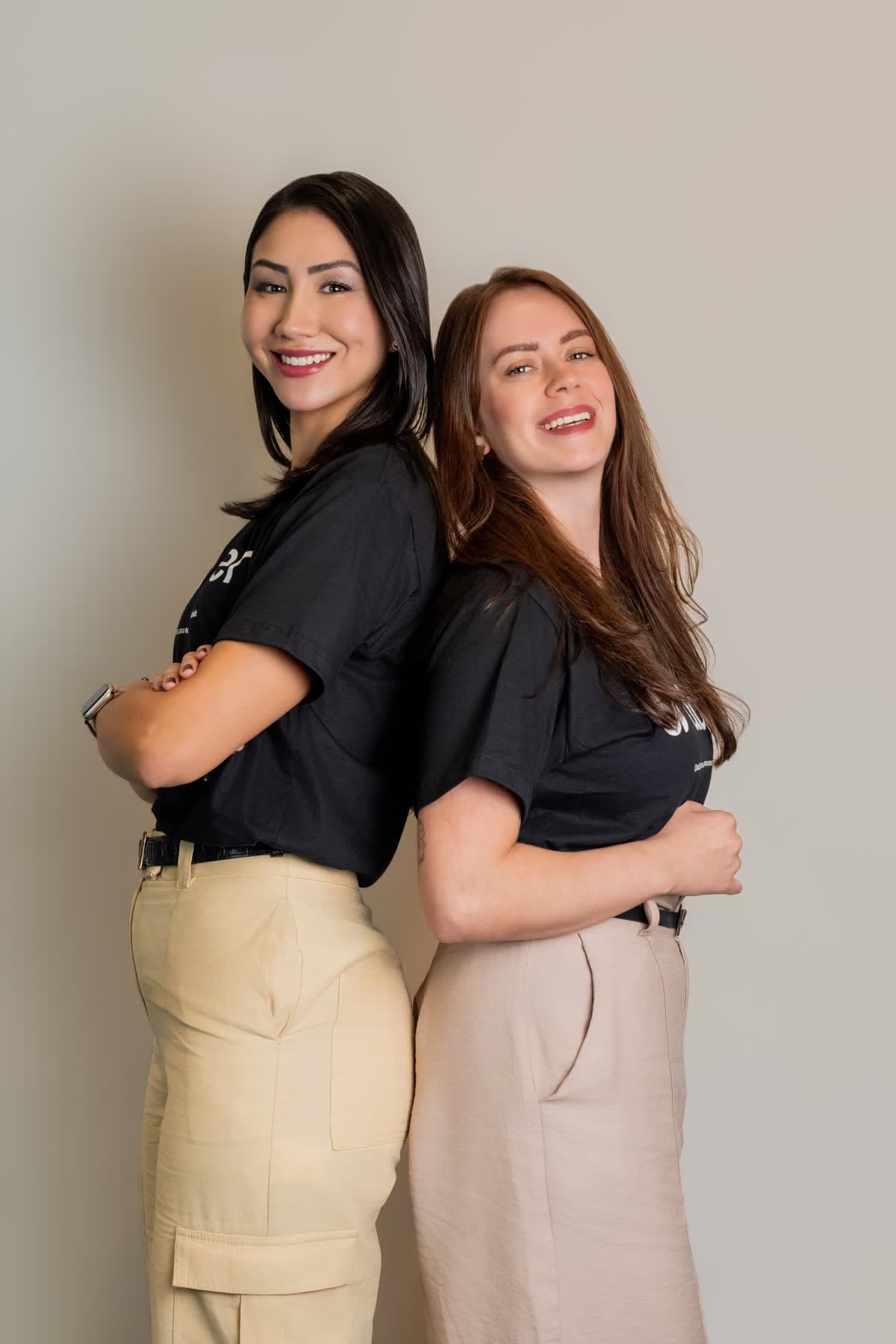 Duas pessoas do time da abler de costas uma para a outra, sorrindo, vestindo camisetas pretas com a marca abler