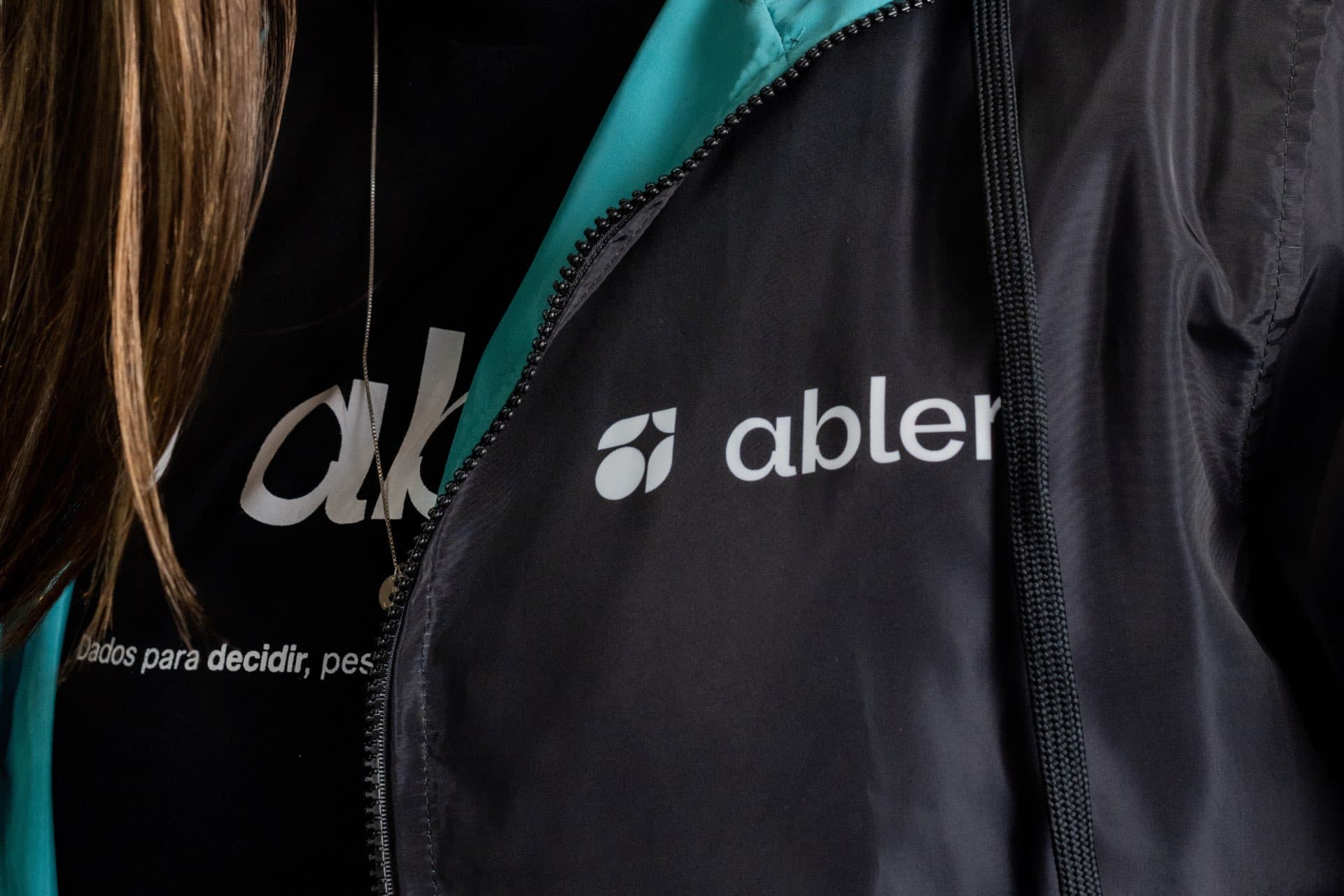 Pessoa vestindo jaqueta e camiseta pretas com o logo e o nome abler